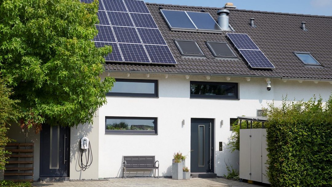 Modernes Einfamilienhaus mit PV-Anlage auf dem Dach und Wallbox vor der Tür.