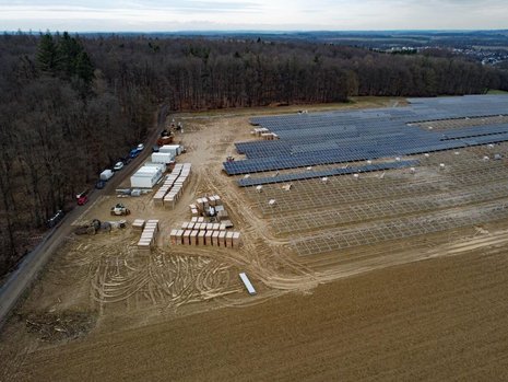 Braunes Feld wird mit Solaranlagen bebaut. Am Rand stehen Baumaterialien und Container.