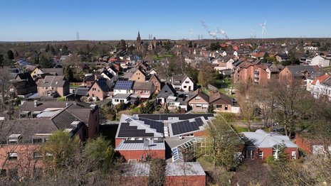 Vogelperspektive auf einen Ort, in dem auf einigen Häusern PV installiert ist. Der Himmel ist blau und wolkenlos.