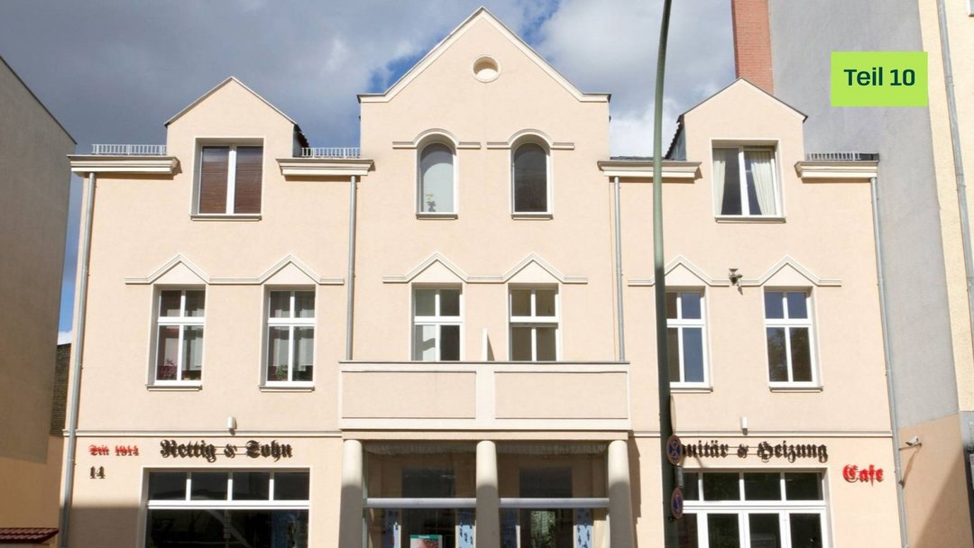 Ein helles Gebäude mit drei Giebeln, davor einzelne grüne Straßenlaterne. Im gelben Kreis steht „Blogserie Teil 10“. Oben rechts: „Green Planet Energy“. Unten sind Ladenschilder zu sehen.