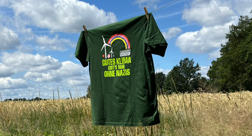 Frau sitzt am Wasser und ist von hinten zu sehen. Auf ihrem grünen T-Shirt steht hinten "Gutes Klima gibt's nur ohne Nazis".