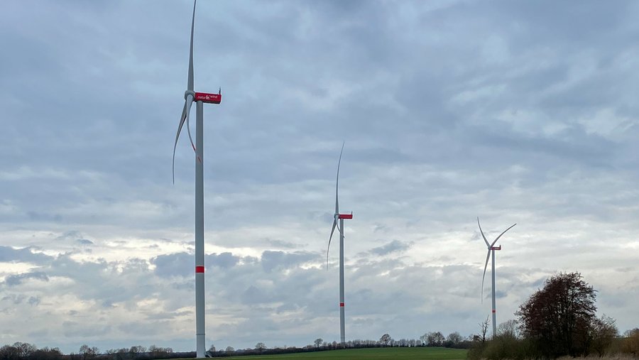 Eine Aufnahme von drei der fünf Windräder in Bälau vor einem wolkigen Himmel.